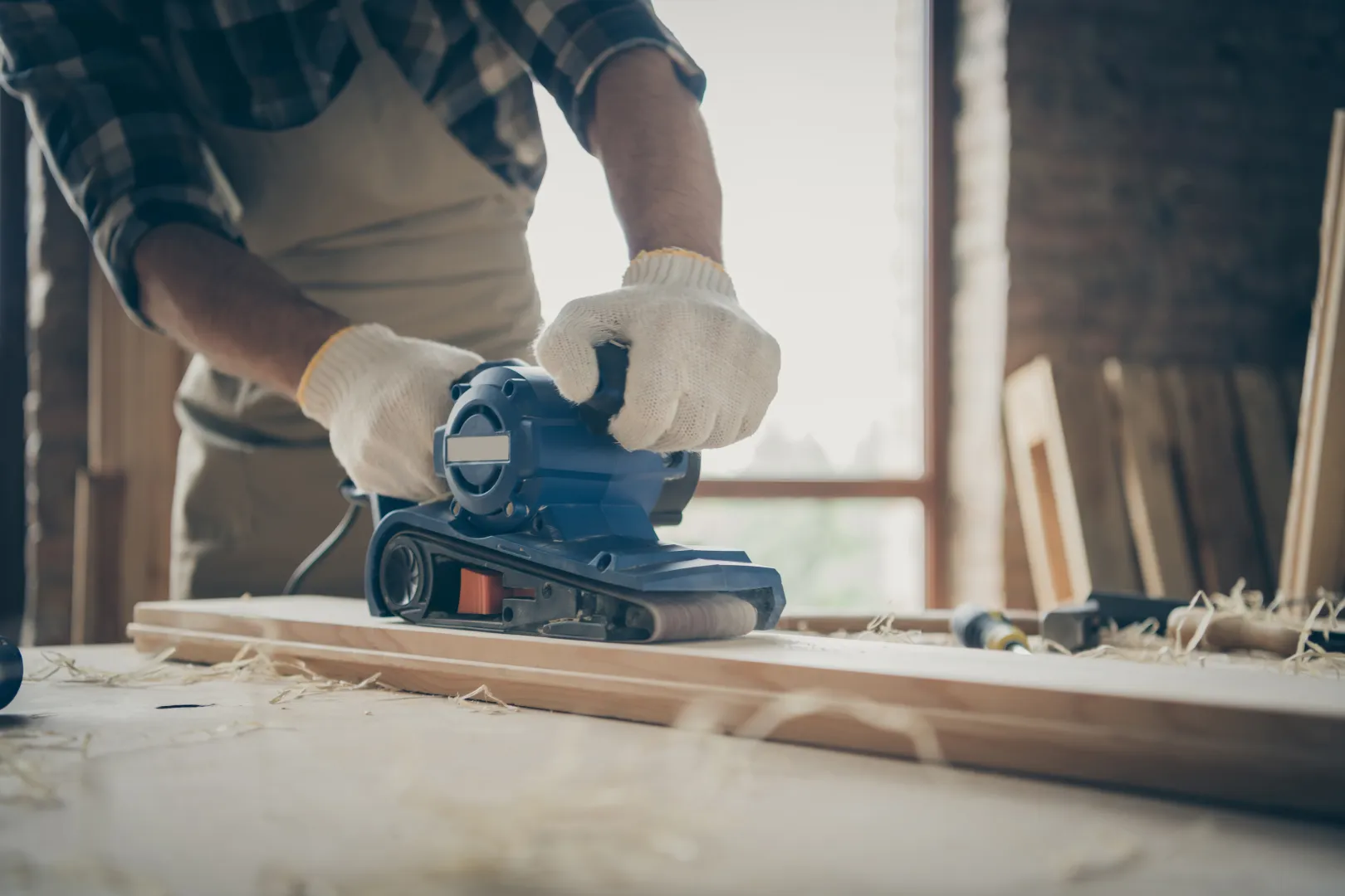cropped-close-up-man-travaillant-avec-du-papier-de-verre-entoure-de-depots-de-traitement-de-bloc-de-bois-avec-les-mains-dans-les-gants